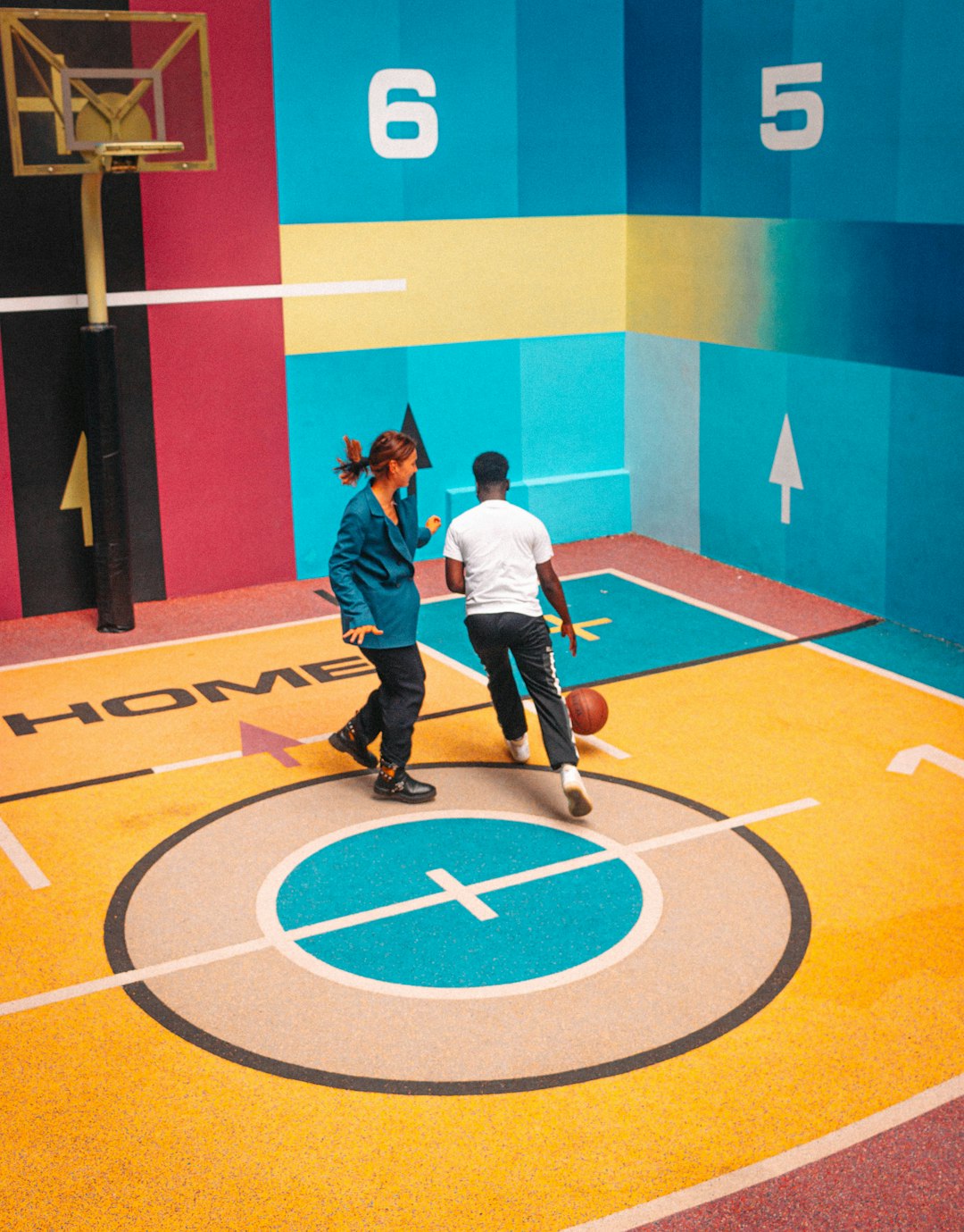 man in white shirt and black pants standing on yellow and blue basketball court