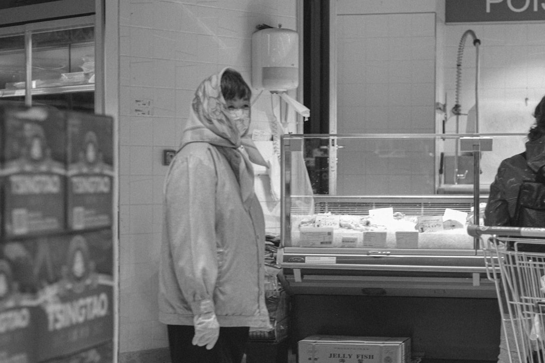 grayscale photo of man in hoodie standing in front of glass window