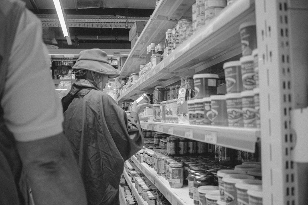 grayscale photo of man in jacket standing in front of shelf