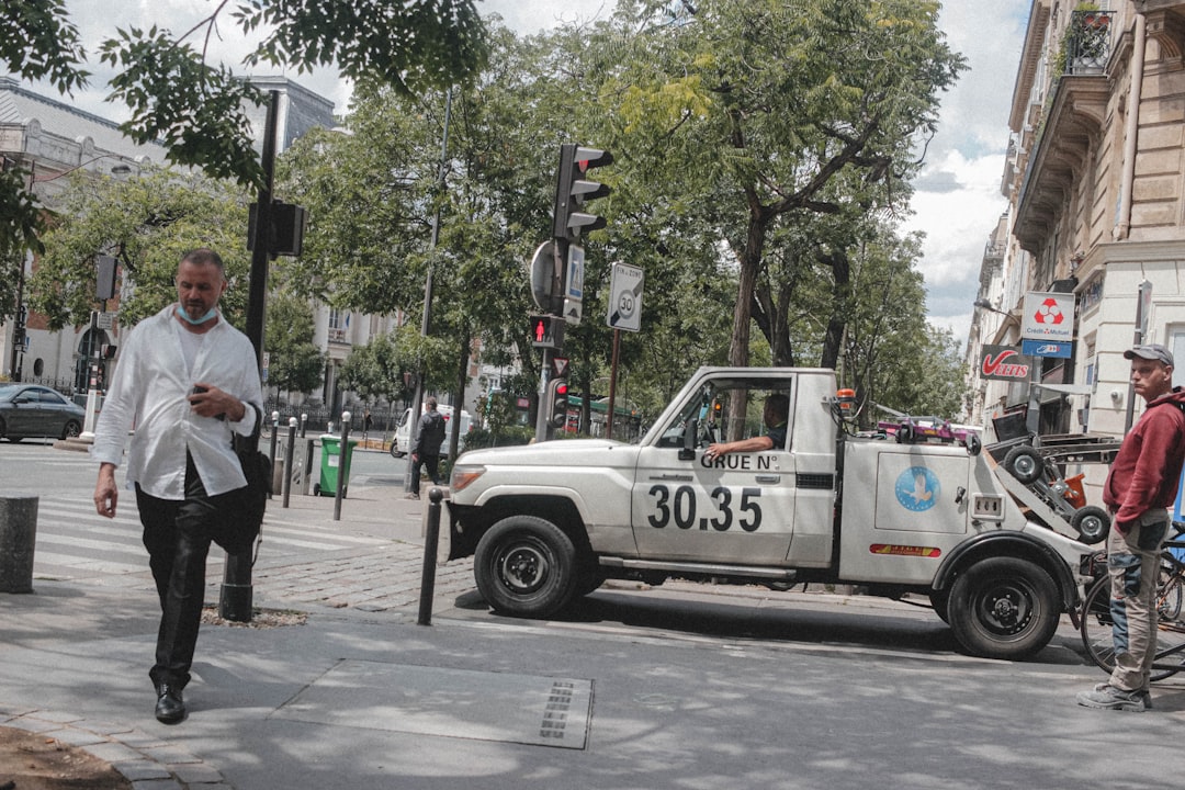 man in white shirt and black pants standing beside white crew cab pickup truck during daytime