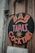 A vintage-style sign with bold, colorful lettering advertising a bar, tapas, and cocktails. The sign is circular and attached to a weathered wooden surface, alongside a mounted menu listing various dishes and prices.
