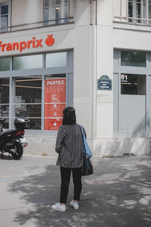 A person wearing a striped outfit stands on the sidewalk in front of a Franprix store. A scooter is parked nearby, and the signage includes promotional posters. The street sign indicates it's Avenue des Gobelins.