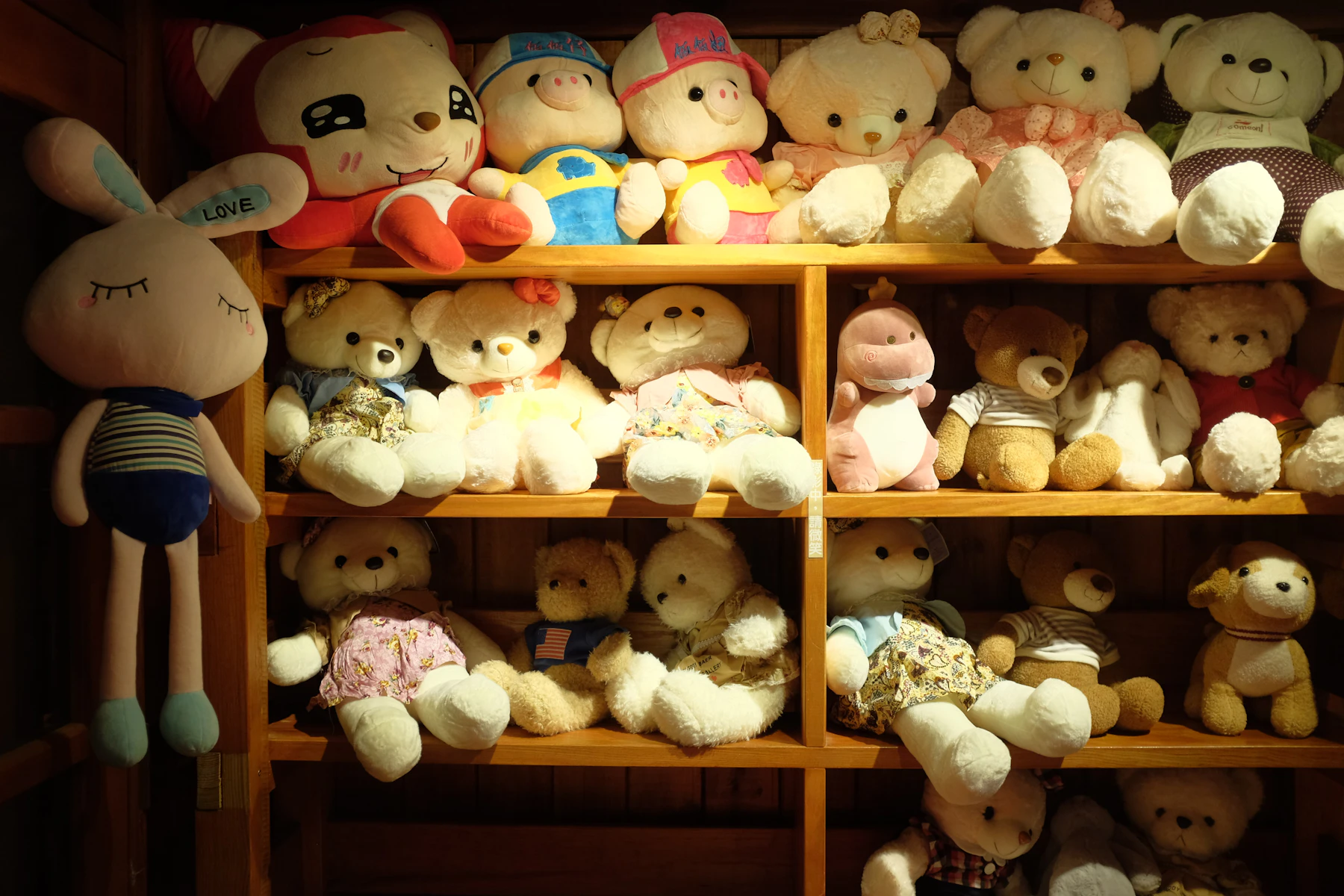 Three wooden shelves lined with teddy bears and other plush toys in small outfits