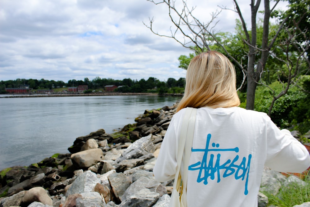 woman in white and blue shirt standing on rocky shore during daytime