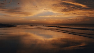 A serene beach sunset with vibrant teal and orange hues reflecting on calm water, inviting relaxation.