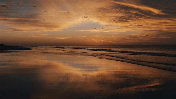 A vibrant sunset over a serene beach with gentle waves reflecting deep navy and sunset orange hues.