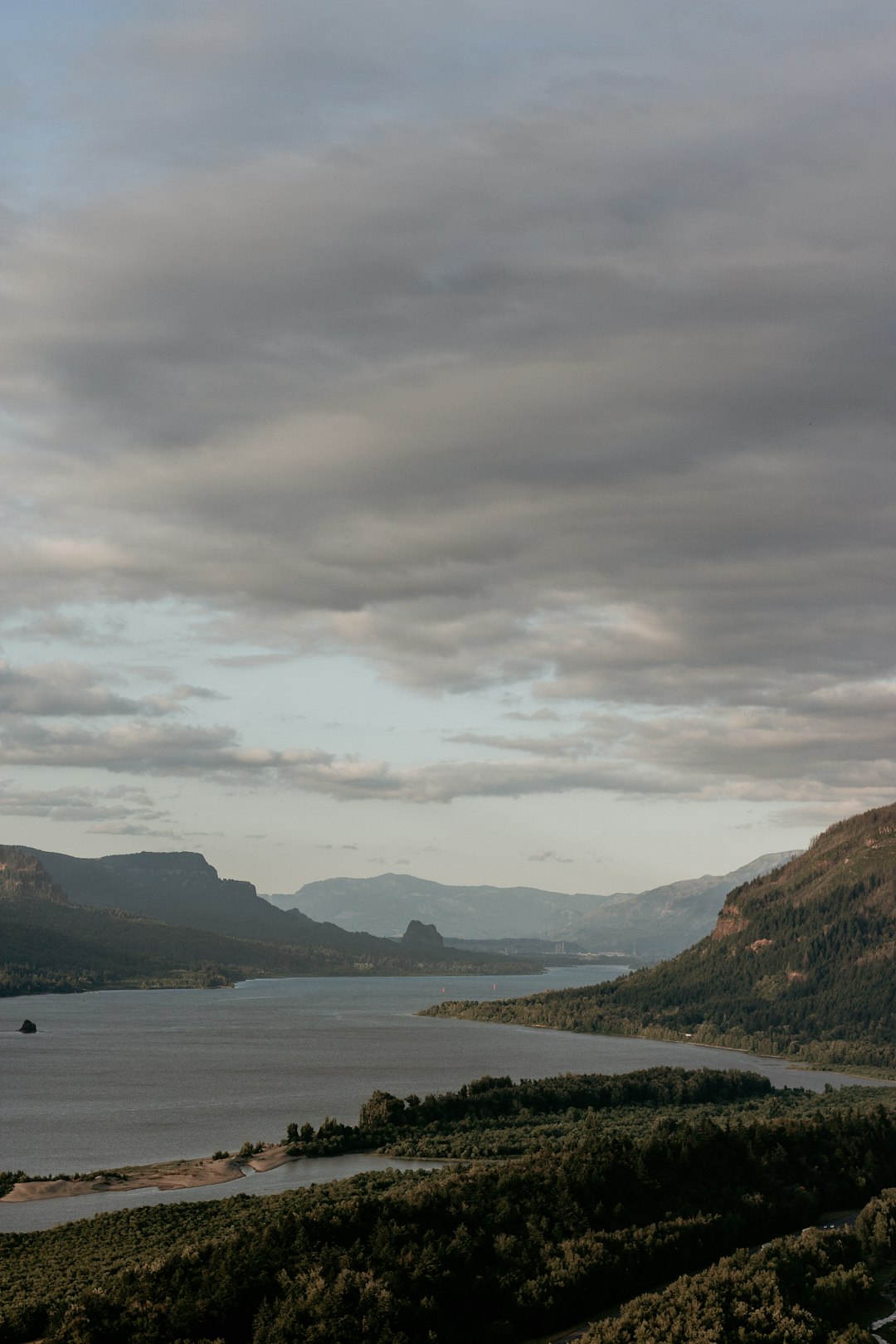 body of water near mountain under cloudy sky during daytime