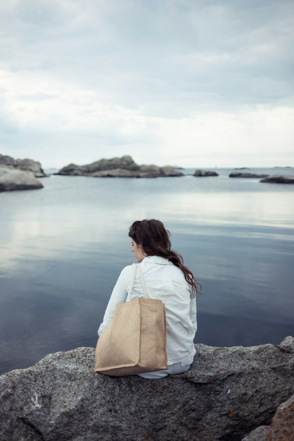 woman in white shirt sitting on rock near body of water during daytime