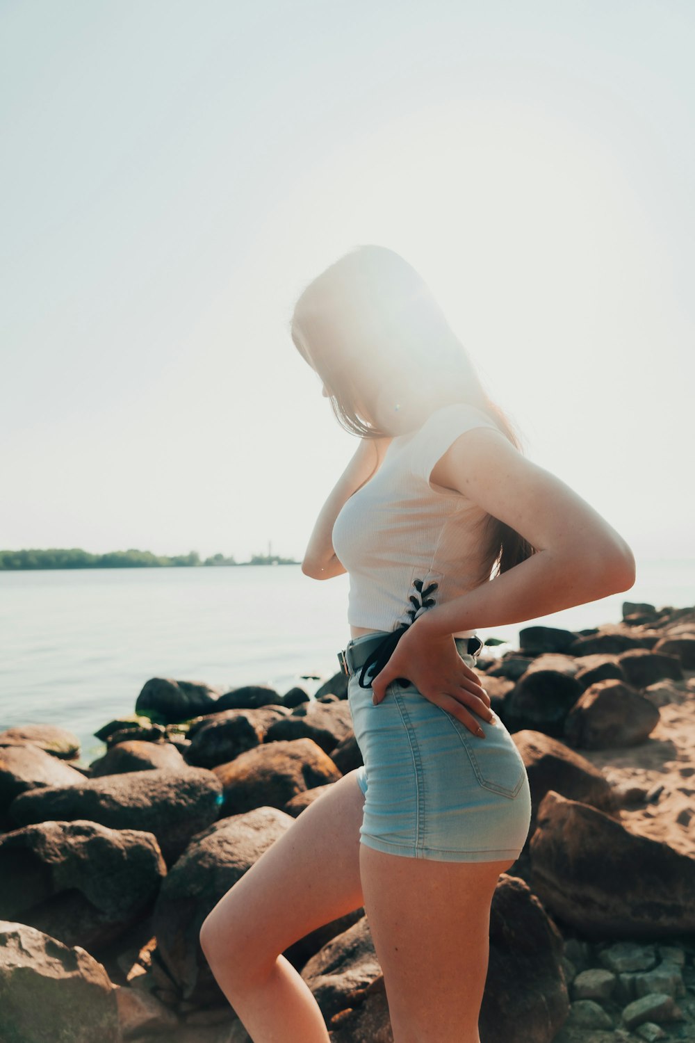 woman in white tank top and blue denim daisy dukes standing on rocky shore during daytime