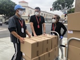 3 men in black polo shirt standing beside brown cardboard boxes