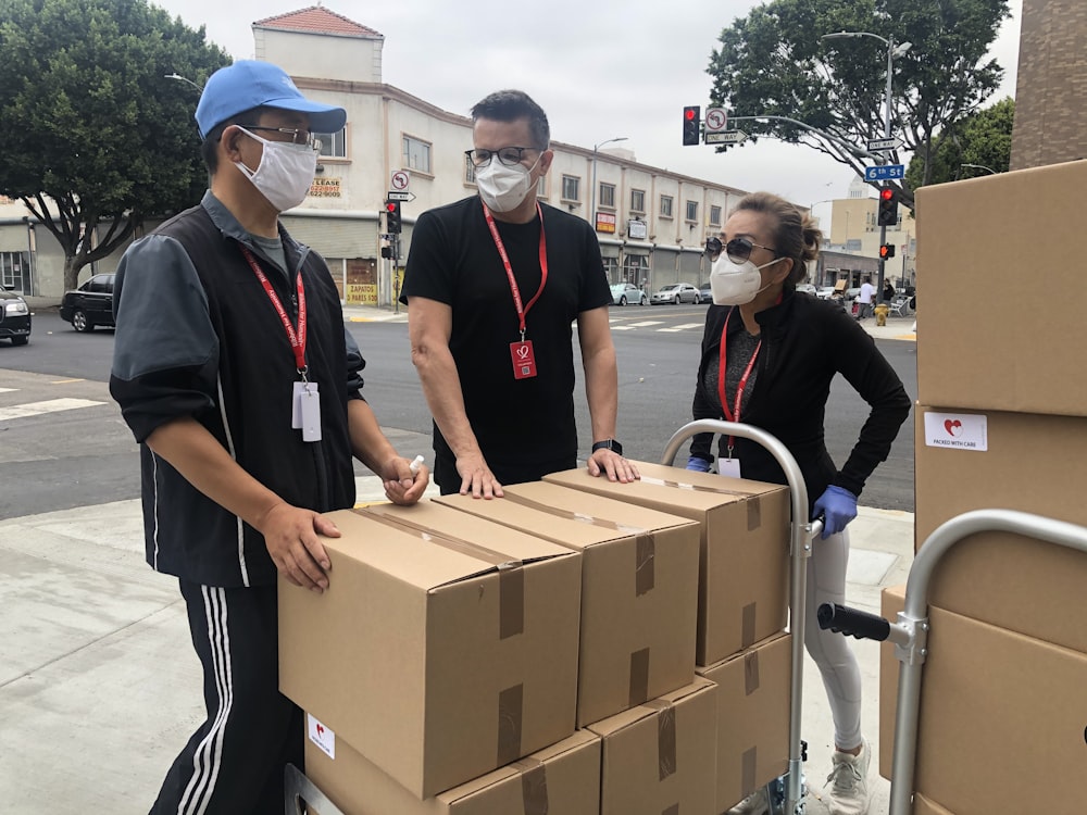 3 men in black polo shirt standing beside brown cardboard boxes