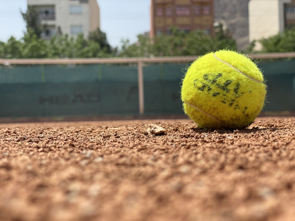 日中の茶色の土に緑のテニスボール