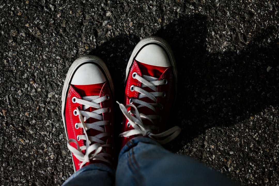 person in blue denim jeans wearing red converse all star high top sneakers