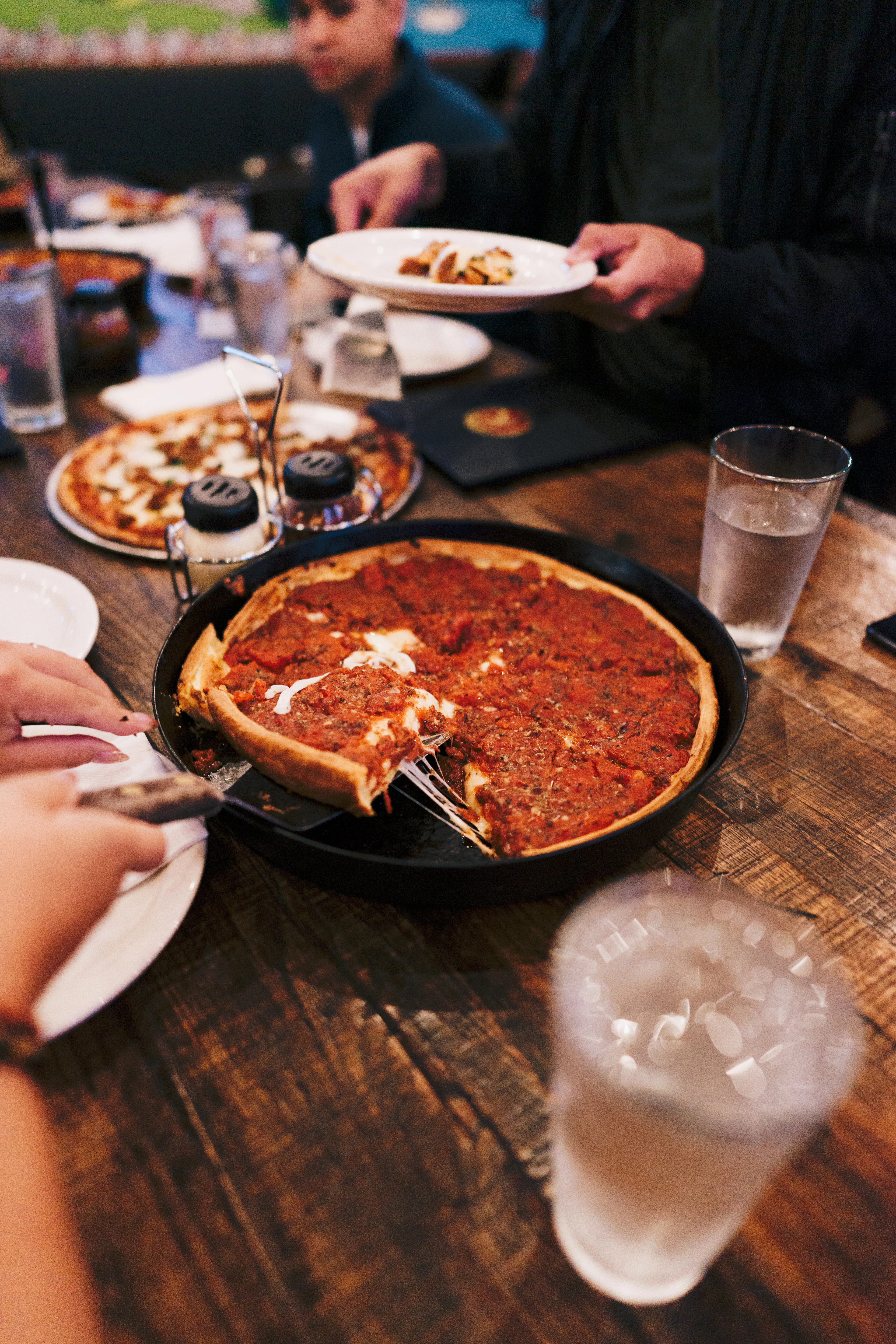 A Chicago deep-dish pizza in its black pan on a wooden table, one slice lifted out