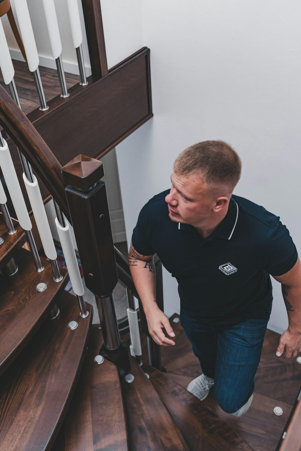 man in black crew neck t-shirt and blue denim jeans standing beside brown wooden staircase