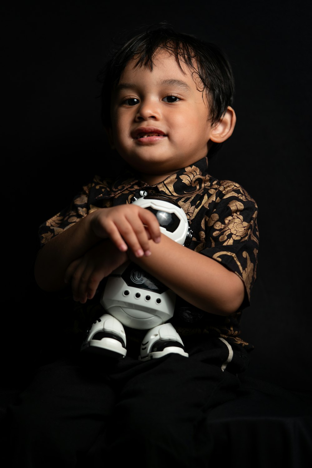 boy in black and white floral shirt holding white and black soccer ball