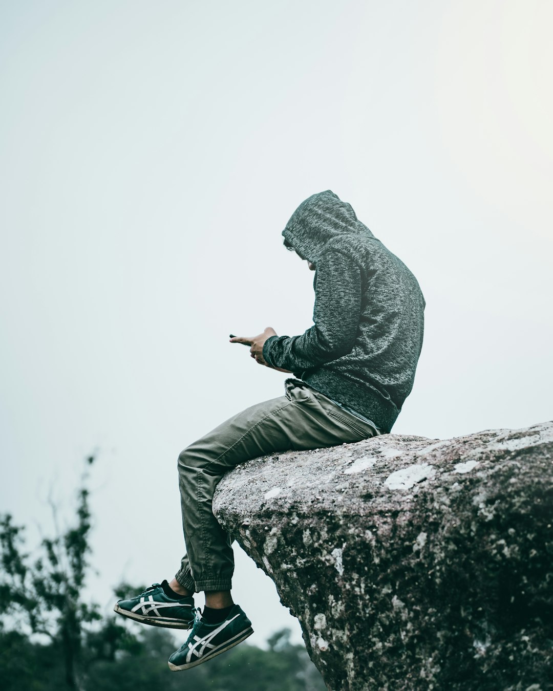 man in black hoodie and gray pants sitting on rock