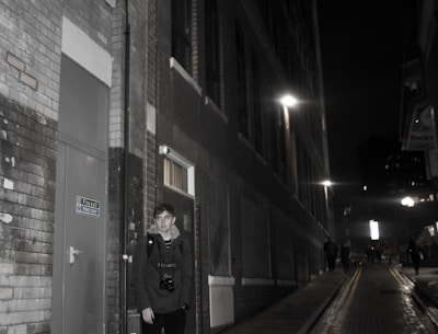 A diverse group of people standing together in a dimly lit urban alley, faces illuminated by soft midnight blue streetlights.