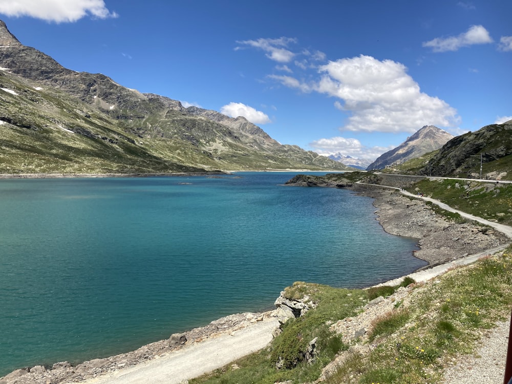 blue body of water near green mountain under blue sky during daytime