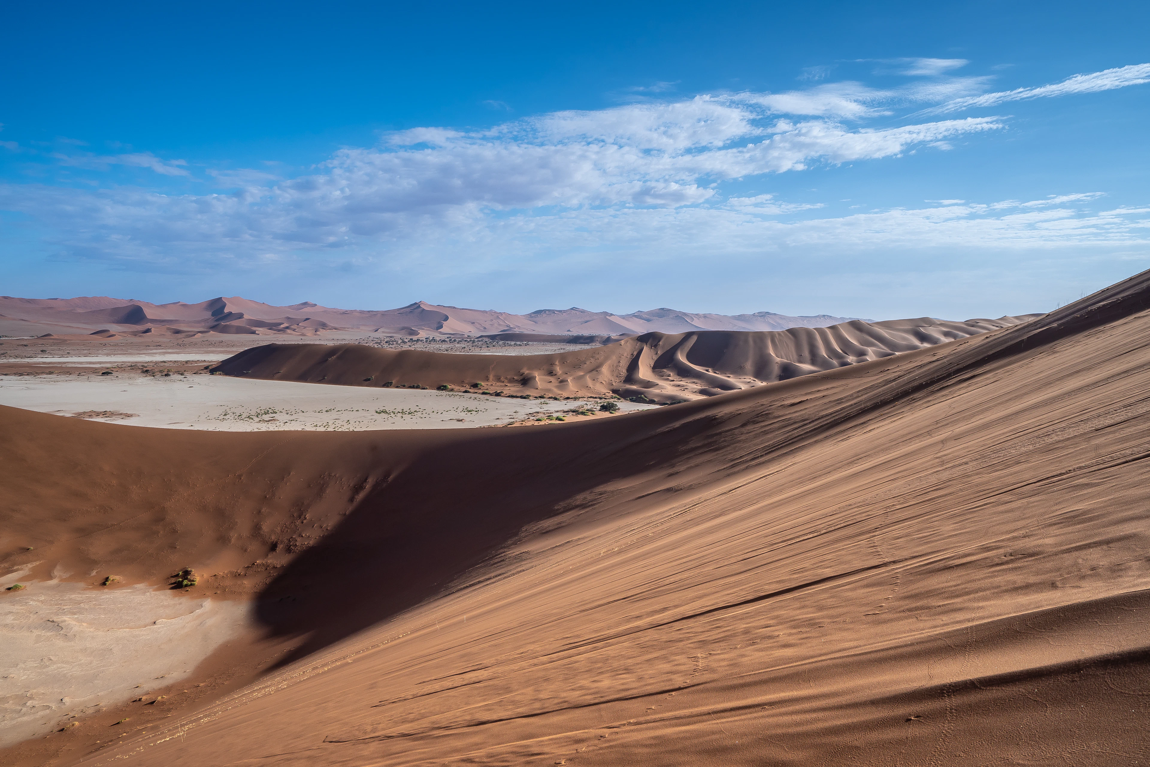 Orange dunes of the Namib Desert and a pale clay pan beneath a blue sky, Sossusvlei, Namibia