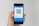 A hand holding a smartphone displaying a QR code on the screen. The interface is primarily blue, indicating a payment or financial app. Above the QR code, there are options related to payment processing.