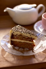 A cozy cafe table displaying a slice of homemade carrot cake with chocolate frosting and a cup of tea.
