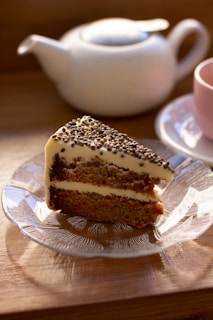 Close-up of a slice of carrot cake on a simple white plate next to a cup of coffee.