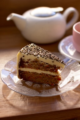 A cozy cafe table displaying a slice of homemade carrot cake with chocolate frosting and a cup of tea.
