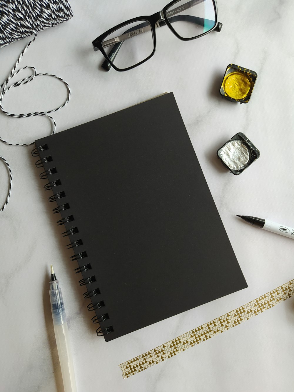 black notebook beside black click pen and black framed eyeglasses
