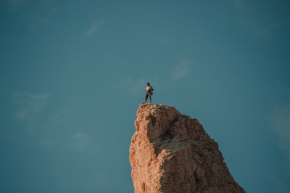 man standing on brown rock formation under blue sky during daytime