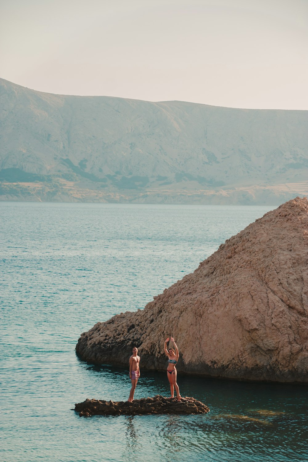 2 women standing on rock near body of water during daytime