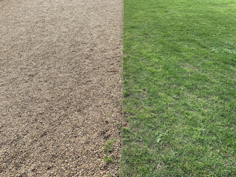 A split landscape with a gravel surface on the left half and a green grass lawn on the right half. The two sections are clearly demarcated and run parallel to each other.