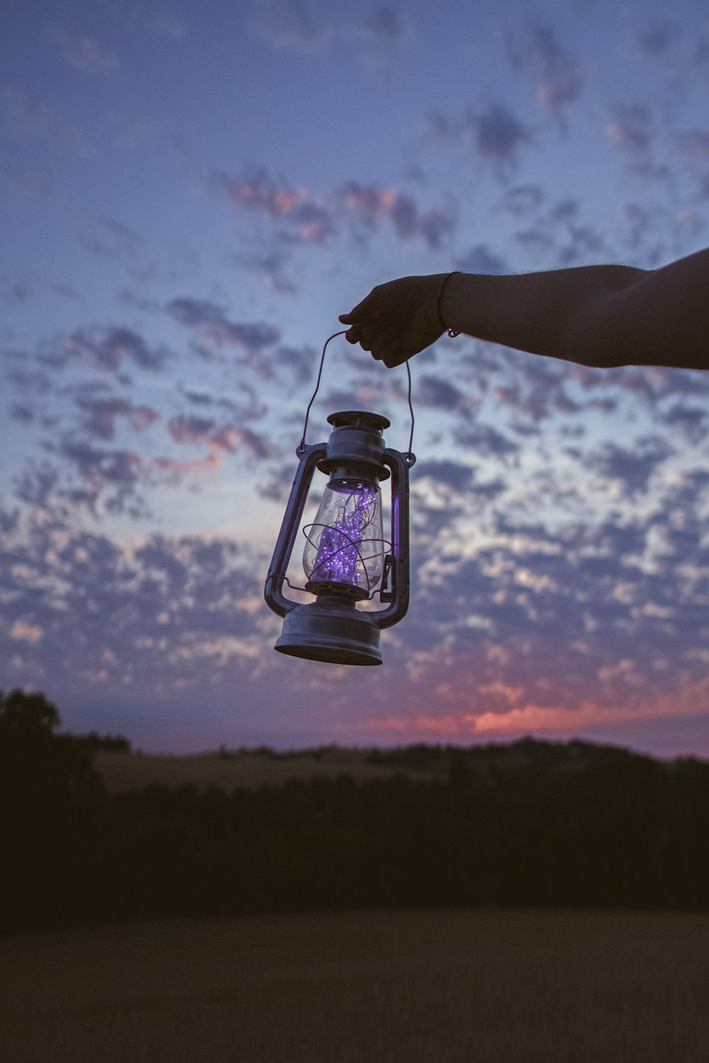 person holding clear glass jar with string lights during sunset