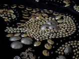 Close-up view of intricate beadwork featuring metallic beads and sequins arranged in a detailed pattern on dark fabric.