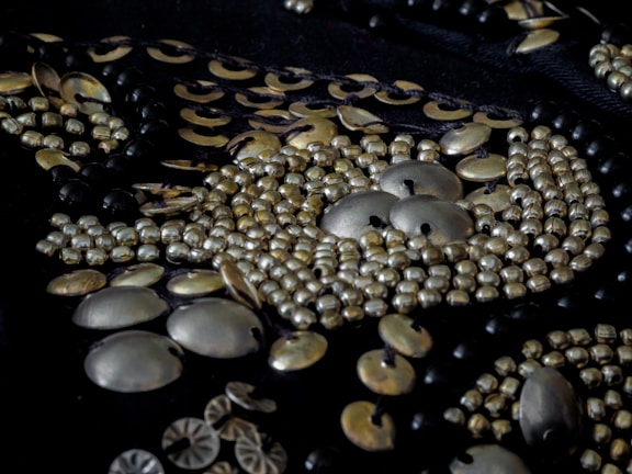 Close-up view of intricate beadwork featuring metallic beads and sequins arranged in a detailed pattern on dark fabric.