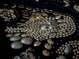 Close-up view of intricate beadwork featuring metallic beads and sequins arranged in a detailed pattern on dark fabric.