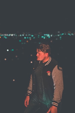 Model wearing a sleek dark grey jacket standing against a shadowy urban backdrop.