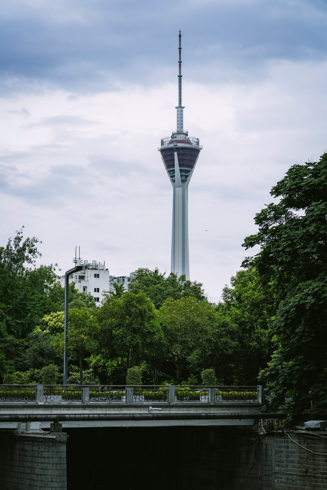 white concrete tower near green trees under white clouds during daytime