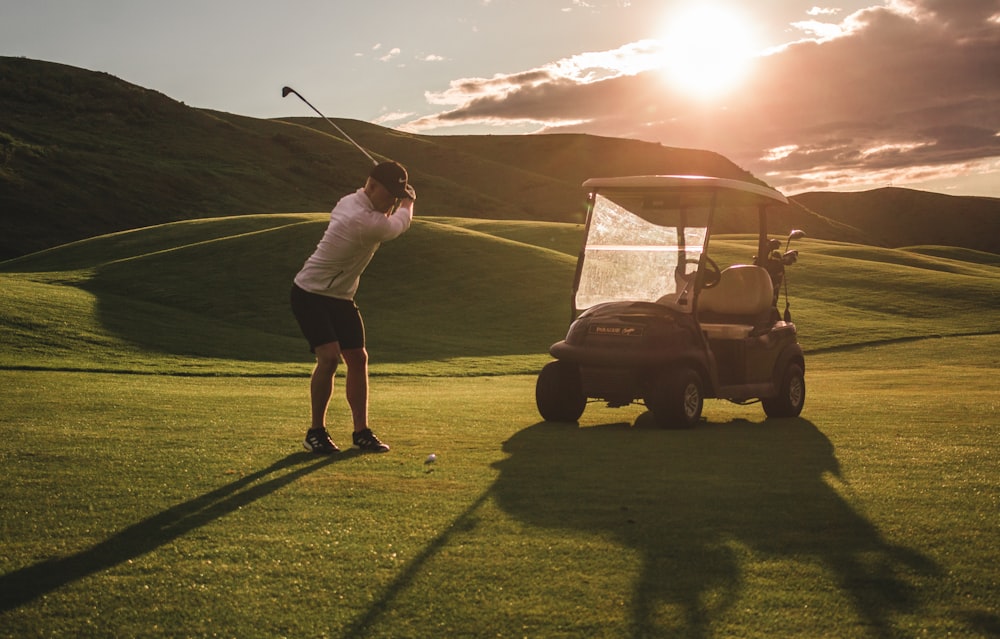 man in white t-shirt and black pants standing on golf cart on green grass field