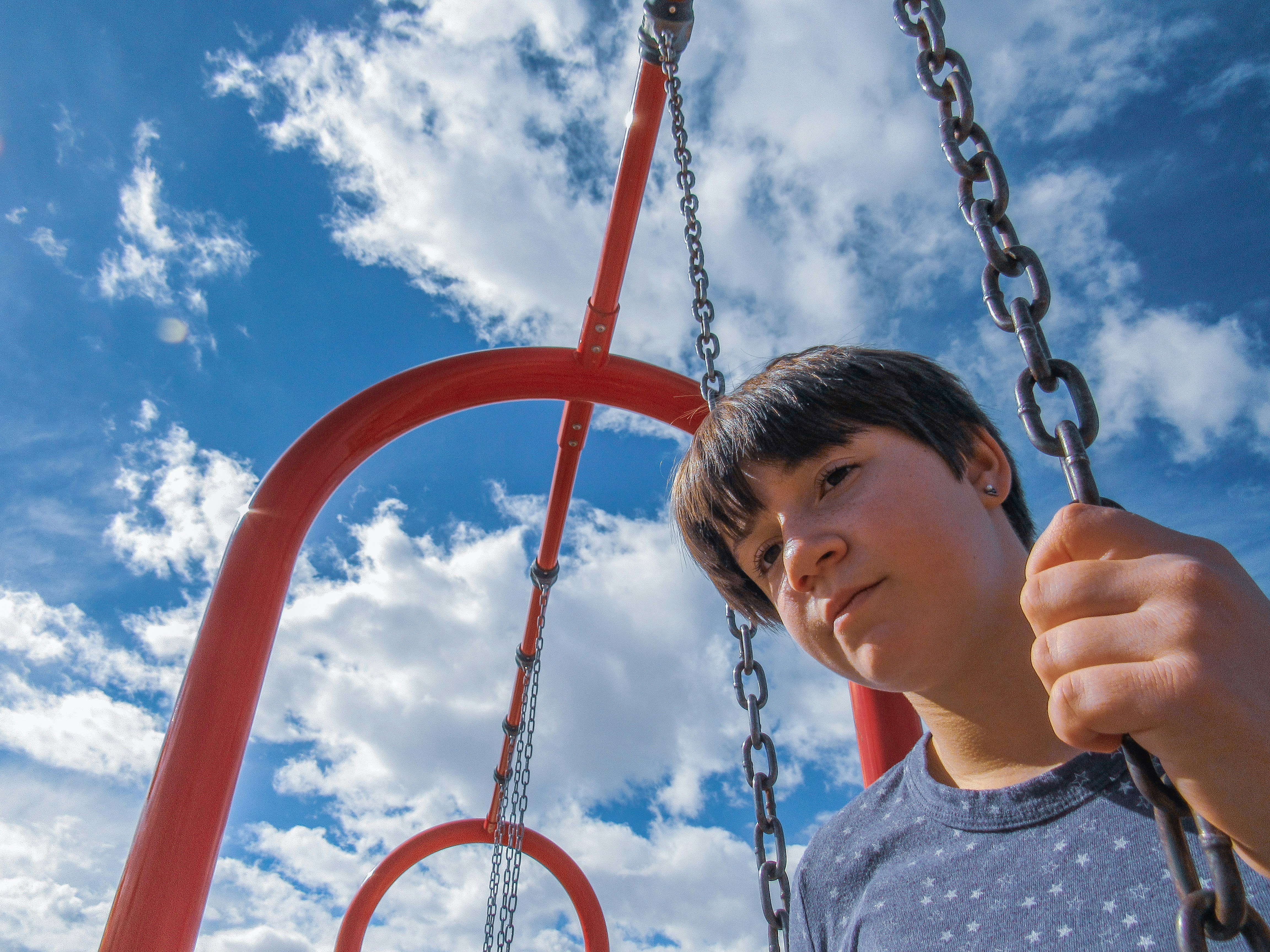 Person sitting on red swing set with blue sky and fluffy white clouds above.