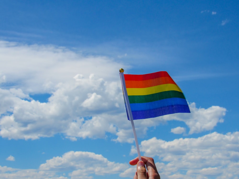 pessoa segurando a bandeira da América sob nuvens brancas e céu azul durante o dia