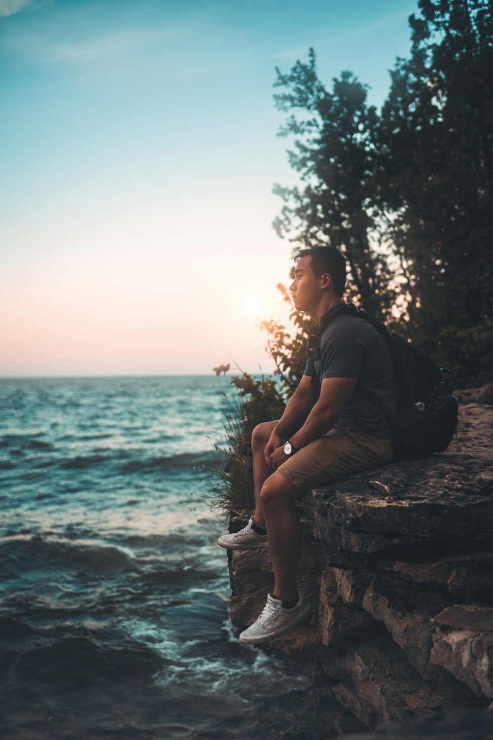 man in black t-shirt sitting on rock near body of water during daytime