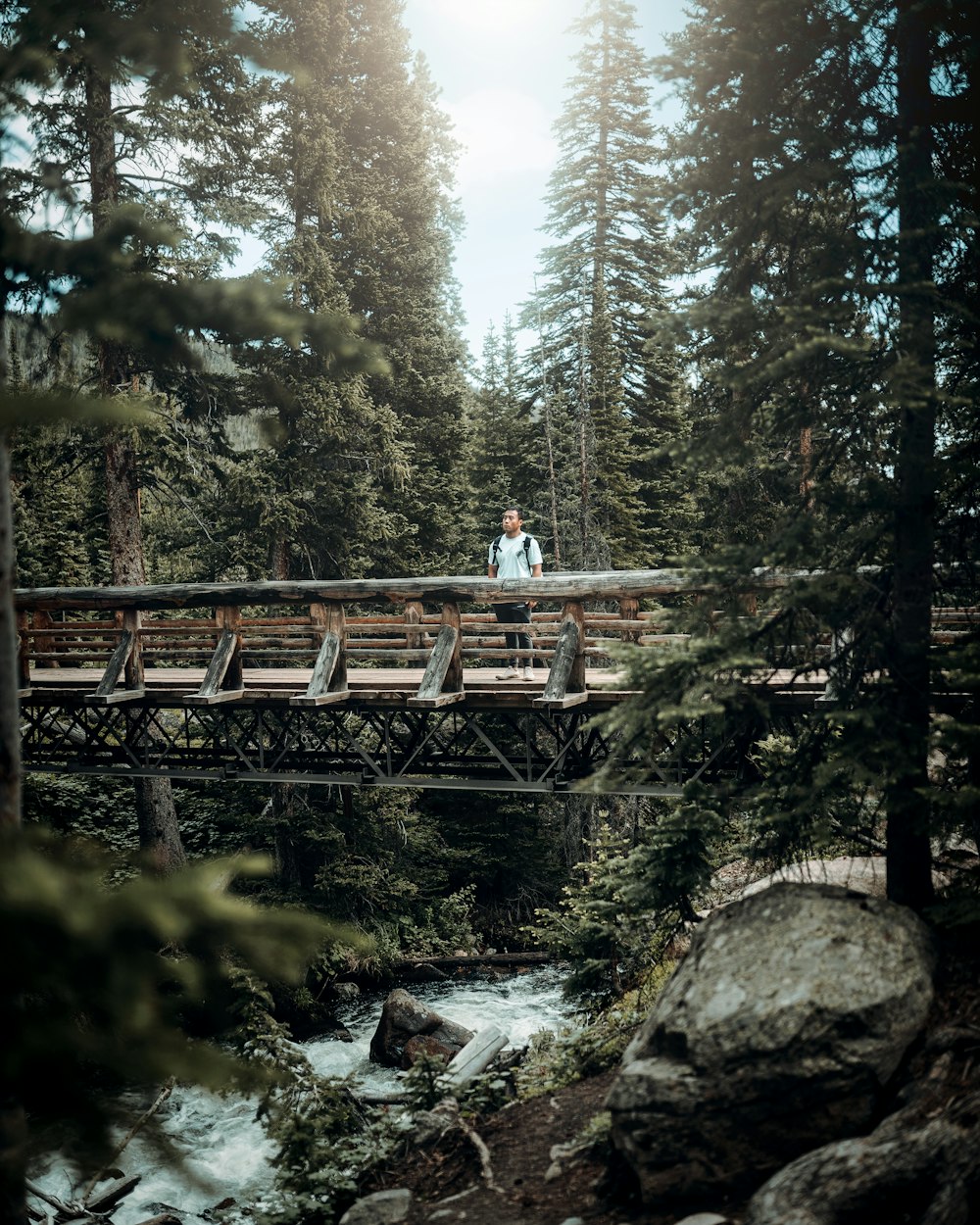 woman in white shirt and black pants standing on brown wooden bridge during daytime