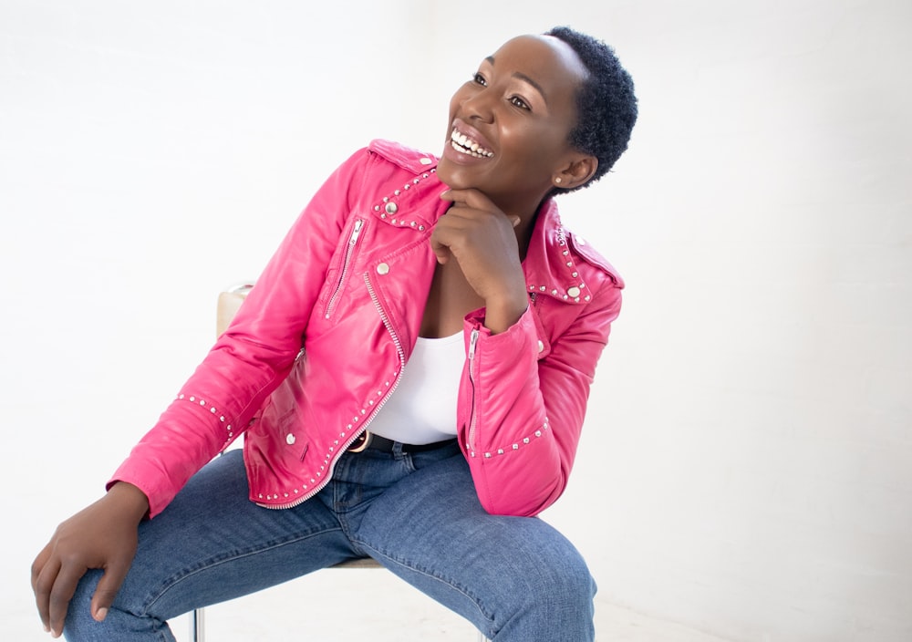 woman in pink leather jacket and blue denim jeans sitting on white floor