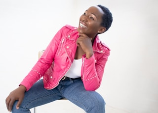 woman in pink leather jacket and blue denim jeans sitting on white floor