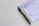 A black and blue pen placed alongside a purple document that appears to contain instructions and a section for signatures. The pen is a retractable ballpoint style with a visible ink chamber and a textured grip. The document includes bold text, bullet points, and a signature area marked with an X.
