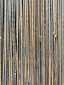 A collection of vertically arranged steel rebar rods displaying a range of rusted and weathered textures. The bars are closely packed and exhibit a pattern of parallel lines and grooves.