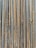 A collection of vertically arranged steel rebar rods displaying a range of rusted and weathered textures. The bars are closely packed and exhibit a pattern of parallel lines and grooves.