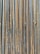 A collection of vertically arranged steel rebar rods displaying a range of rusted and weathered textures. The bars are closely packed and exhibit a pattern of parallel lines and grooves.