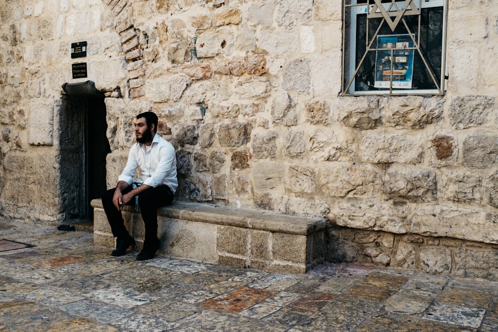 man in white dress shirt sitting on brown concrete wall during daytime